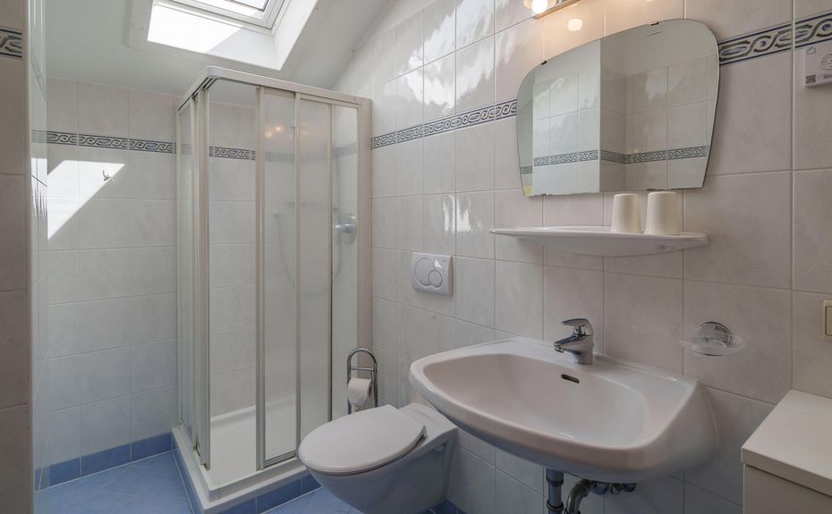 Small bathroom with corner shower, white toilet, wall-mounted white sink, and a mirror with two lights above it.