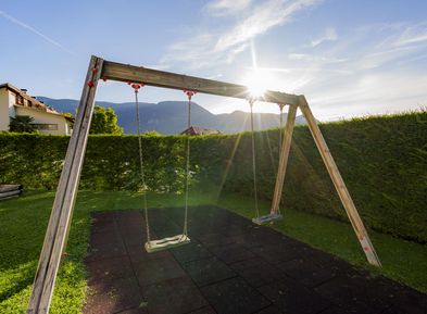 Bambini che giocano su un'altalena nel giardino degli appartamenti Wieserhof ad Andriano, vacanze in famiglia sulla Strada del Vino dell'Alto Adige